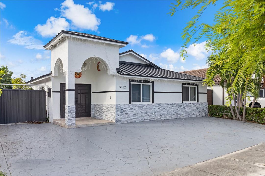 Single-story exterior featuring a metal roof, arched covered entryway, stone-veneer accent siding, and a decorative front door