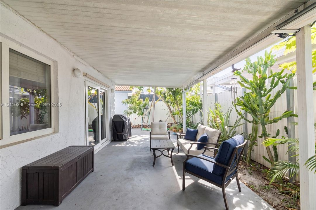 Covered patio featuring a concrete floor, stucco exterior wall, sliding glass door, and perimeter fencing