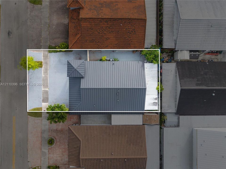 Aerial perspective of a property featuring a metal roof, a corner turret, and a concrete driveway