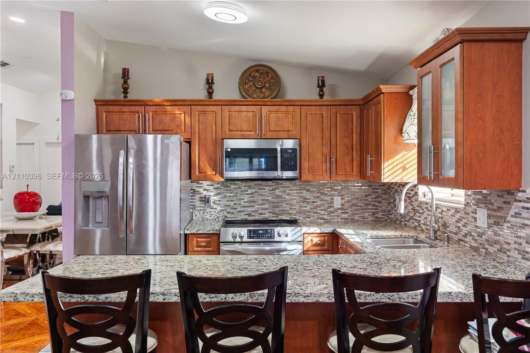 Kitchen featuring wood cabinetry, stone countertops, mosaic tile backsplash, and stainless steel appliances