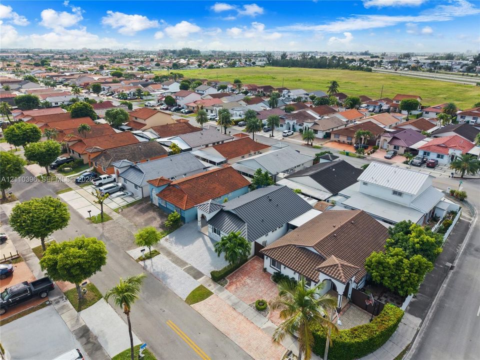 Aerial perspective of a suburban neighborhood featuring paved streets, mature trees, diverse roof styles, and proximity to expansive open green space