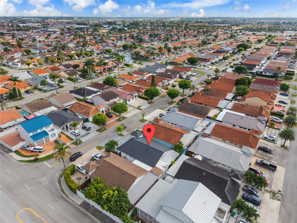 Aerial perspective of a corner lot property featuring a dark-toned roof, concrete driveway, and established landscaping