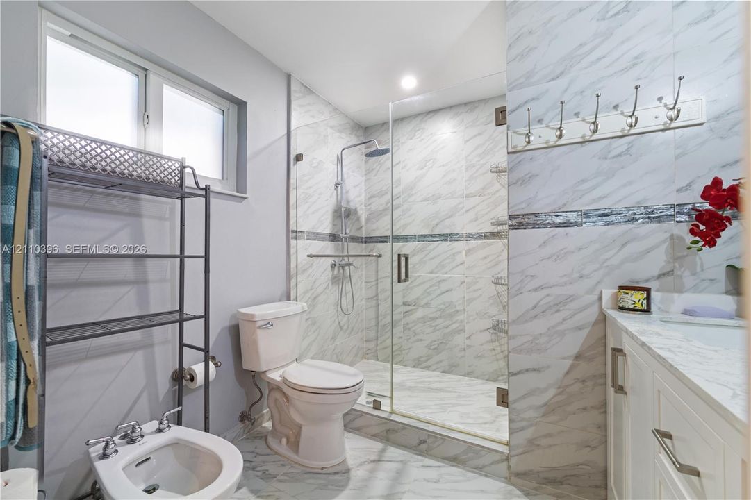 Walk-in shower with floor-to-ceiling stone-patterned tile, glass enclosure, vanity with stone-patterned countertop, and bidet