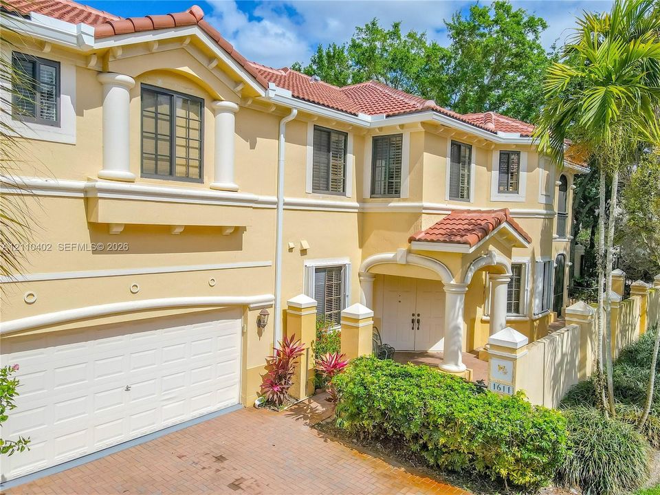 Mediterranean-inspired exterior featuring a clay tile roof, stucco facade, decorative columns, brick-paved driveway, and integrated two-car garage