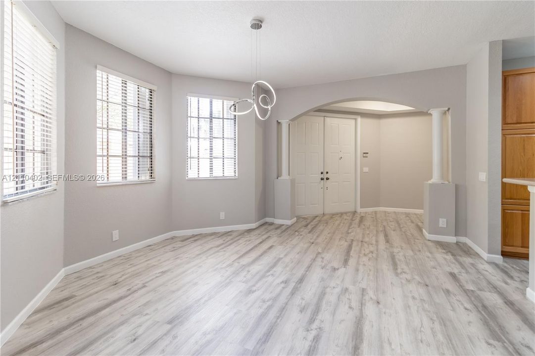 Wood-finish flooring, arched entryway with architectural columns, contemporary geometric pendant lighting, and multiple windows with horizontal blinds