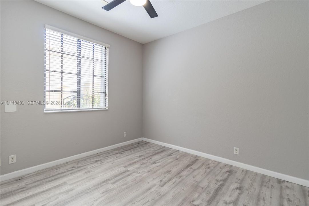 Room featuring wood-finish flooring, neutral wall paint, a multi-pane window with horizontal blinds, and a matte black ceiling fan