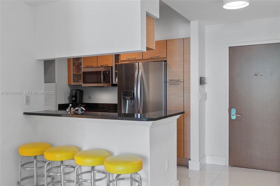 Kitchen featuring a pass-through breakfast bar with stone surfacing, stainless steel appliances, and wood-finish cabinetry