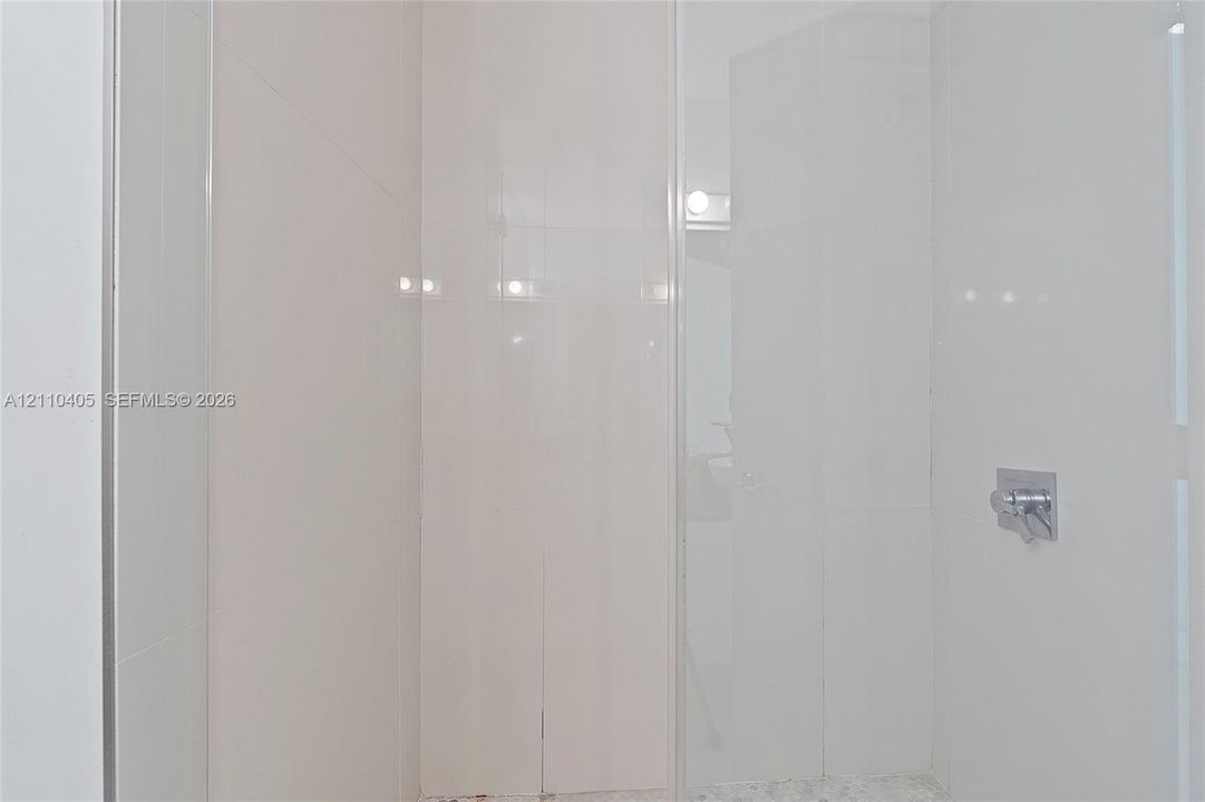 Walk-in shower enclosure with full-height white tile wall surround, glass door, and polished chrome fixtures