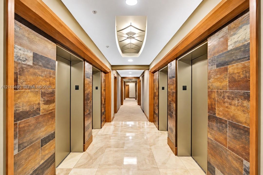 Elevator lobby featuring metallic elevator doors, stone-tiled accent walls, wood trim detailing, recessed architectural lighting, and polished stone flooring