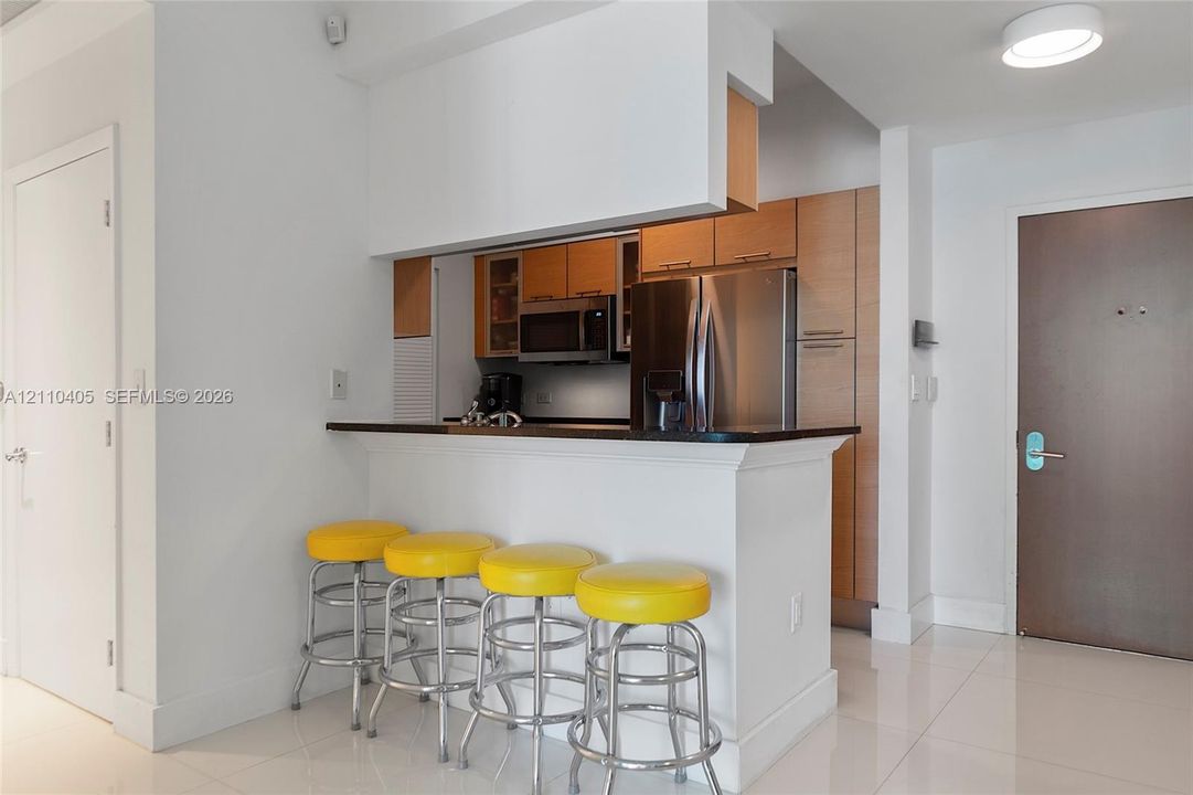 Kitchen featuring wood-finish cabinetry, stainless steel appliances, dark stone-surface breakfast bar, and polished tile flooring