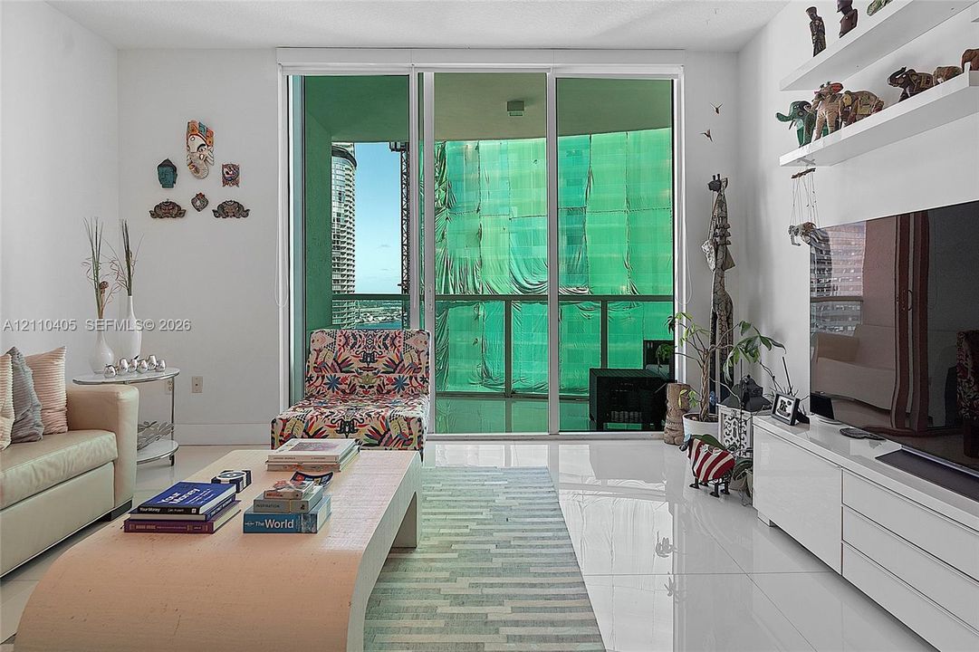 Living area featuring floor-to-ceiling glass sliding doors, built-in white wall shelving, polished tile flooring, and a private balcony
