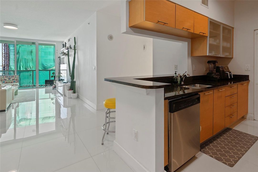Kitchen featuring cabinetry with a light wood finish, dark stone countertops, stainless steel dishwasher, and polished light-colored flooring