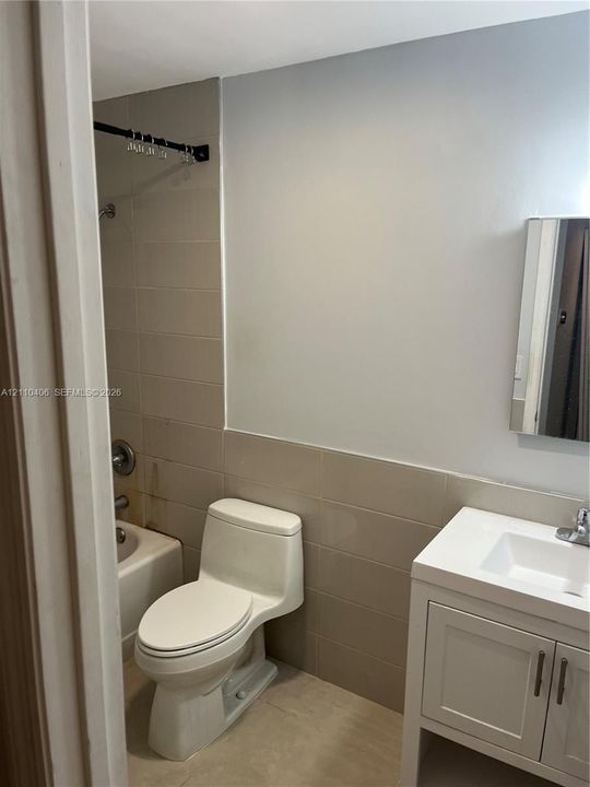 Bathroom featuring a white vanity cabinet with a stone-top integrated sink, a one-piece toilet, and tile wall surrounds with an integrated bathtub