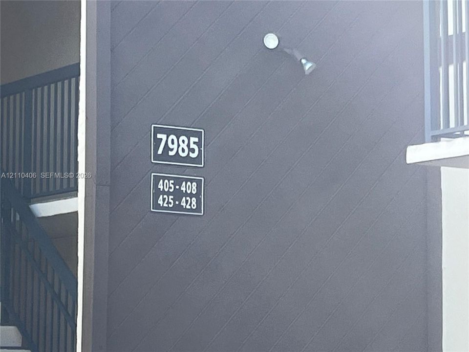 Exterior facade featuring diagonal siding, wall-mounted light fixture, and unit signage