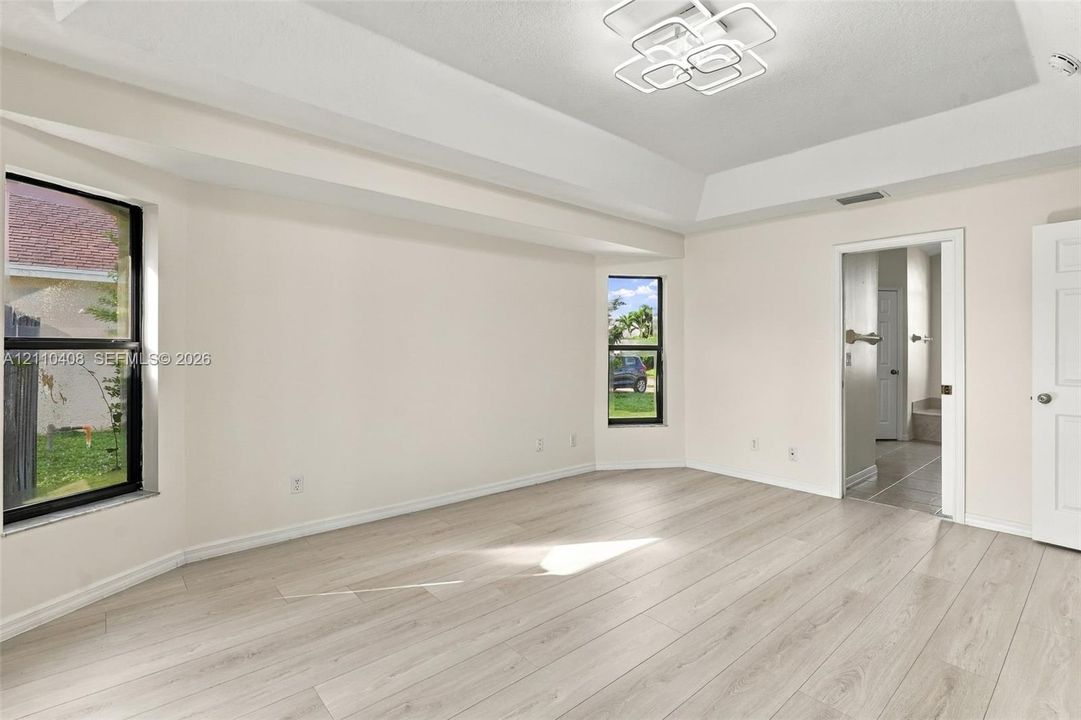 Room featuring a tray ceiling, wood-finish flooring, dual windows, and a multi-tiered geometric LED light fixture