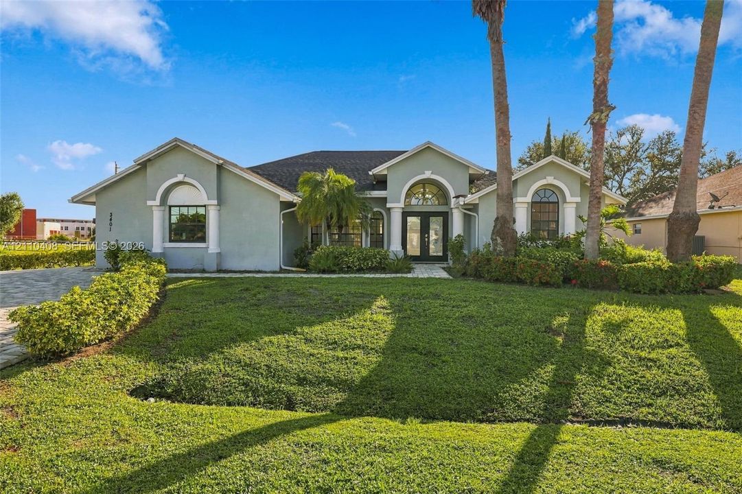 Single-story exterior featuring a light-toned stucco façade, arched window surrounds, a paved stone driveway, and an arched entry with double doors