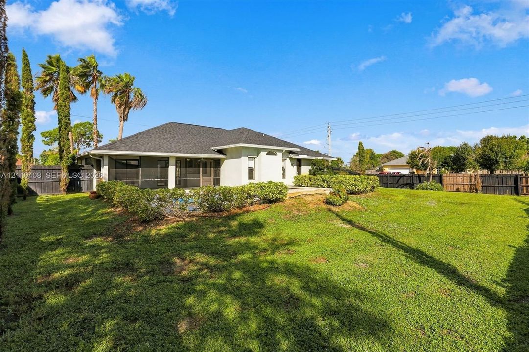 Rear exterior featuring a large grassy lawn, a screened-in lanai, mature palm trees, and a wooden perimeter fence
