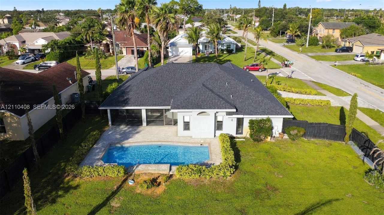 Single-story residence featuring a dark shingle hip roof, a screened rear lanai, a concrete paver pool deck, a rectangular swimming pool, and a perimeter privacy fence