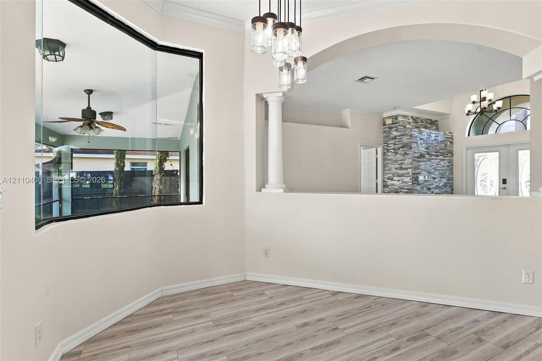 Bay window featuring floor-to-ceiling glass, wood-finish flooring, architectural column, arched wall opening, and multi-light pendant fixture