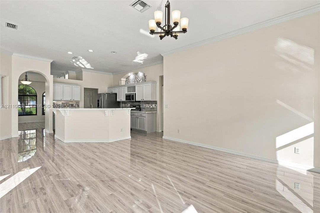 Open-concept space featuring polished wood-finish flooring, white cabinetry, a kitchen island, recessed lighting, and a multi-arm chandelier