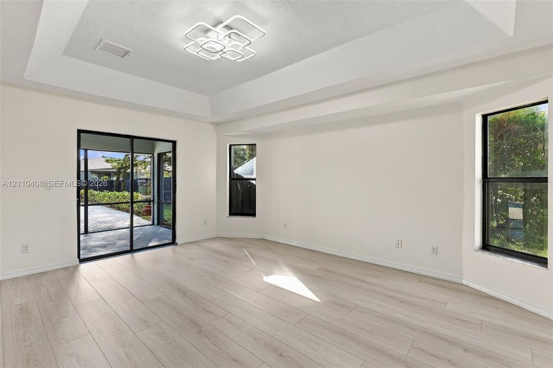Tray ceiling featuring a geometric flush-mount light fixture, light wood-finish flooring, and sliding glass doors with black frames
