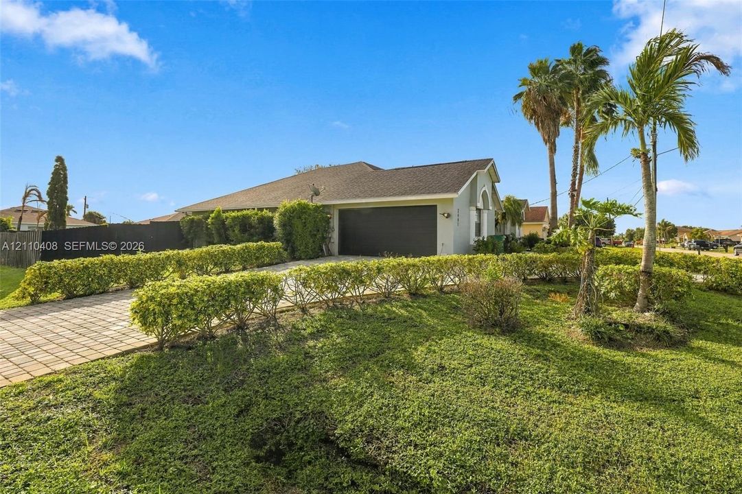 Single-story residence featuring a shingled roof, paver driveway, attached two-car garage, and established tropical landscaping