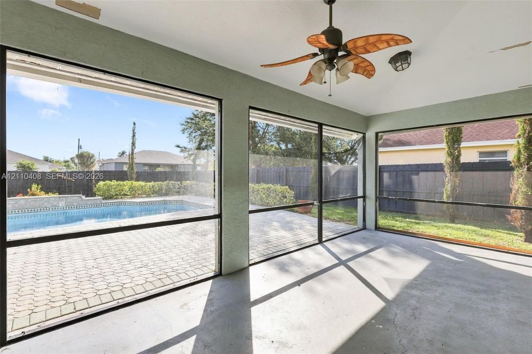 Screened-in patio featuring a vaulted ceiling with a palm-blade paddle fan, concrete flooring, large window panels, and direct exposure to a paved pool deck