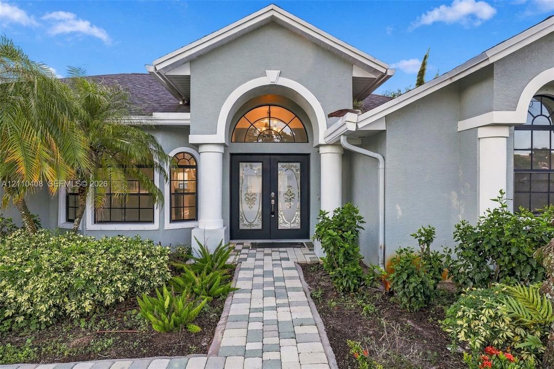 Stucco exterior featuring dual columns, a stone paver walkway, double front entry doors with decorative glass inserts, and a prominent arched transom window
