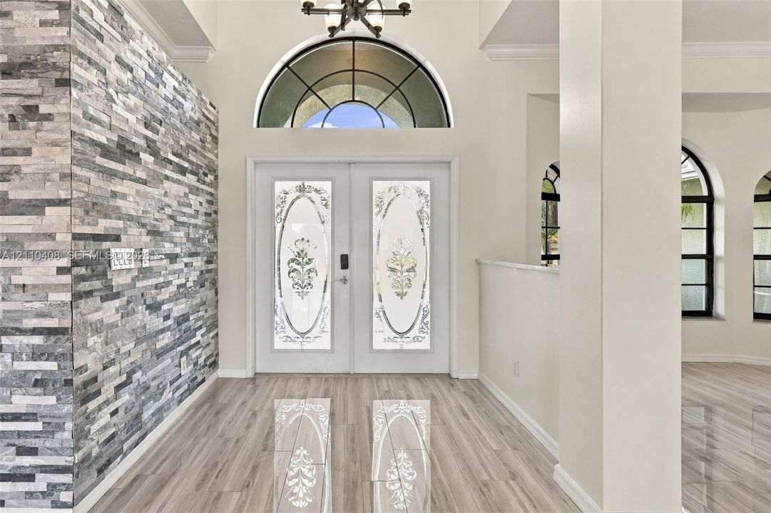 Entryway featuring a stacked stone accent wall, double doors with decorative glass inserts, a semicircular transom window, and wood-finish flooring