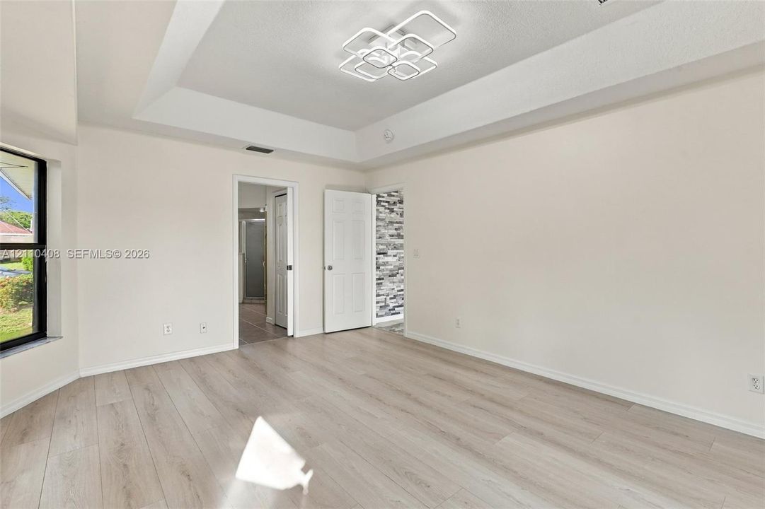Tray ceiling featuring a geometric LED light fixture, complemented by wood-finish flooring and neutral wall tones