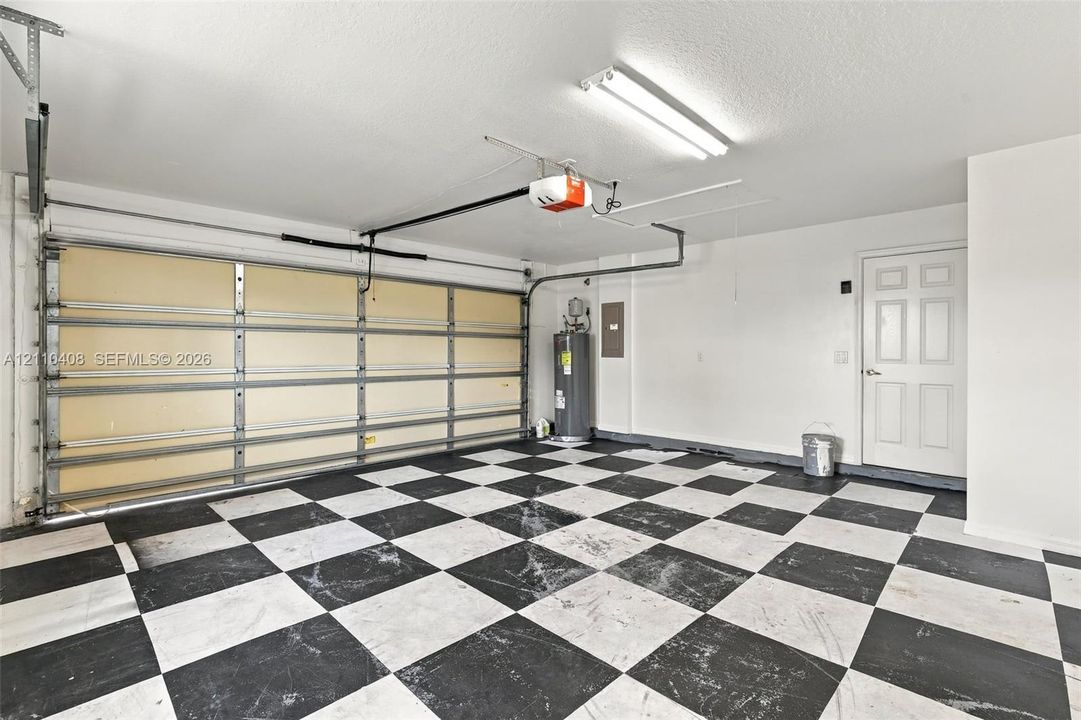 Garage featuring a black and white checkered floor, automatic garage door opener, overhead fluorescent lighting, and an internal water heater