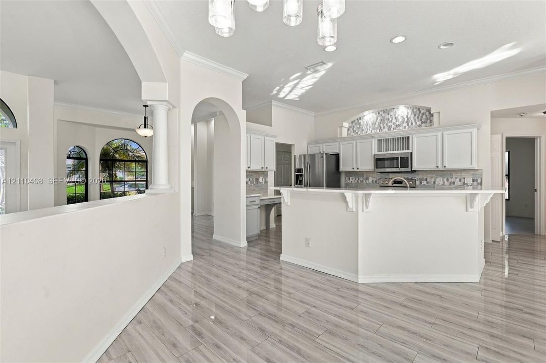 Kitchen featuring wood-finish tile flooring, white cabinetry, a breakfast bar with decorative corbels, stainless steel appliances, and arched architectural entryways