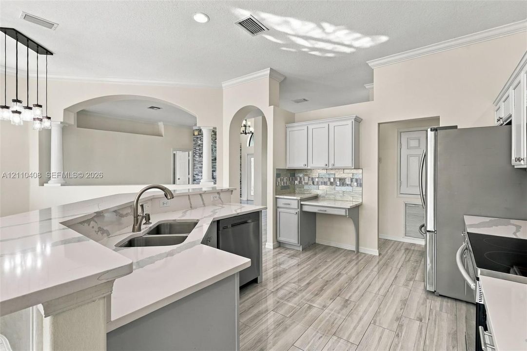 Kitchen featuring quartz countertops, wood-finish flooring, stainless steel appliances, decorative tile backsplash, and arched architectural detailing