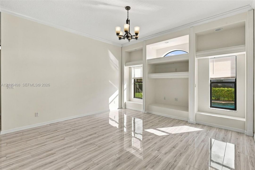 Room featuring wood-finish tile flooring, custom built-in cabinetry, crown molding, and a central multi-light chandelier