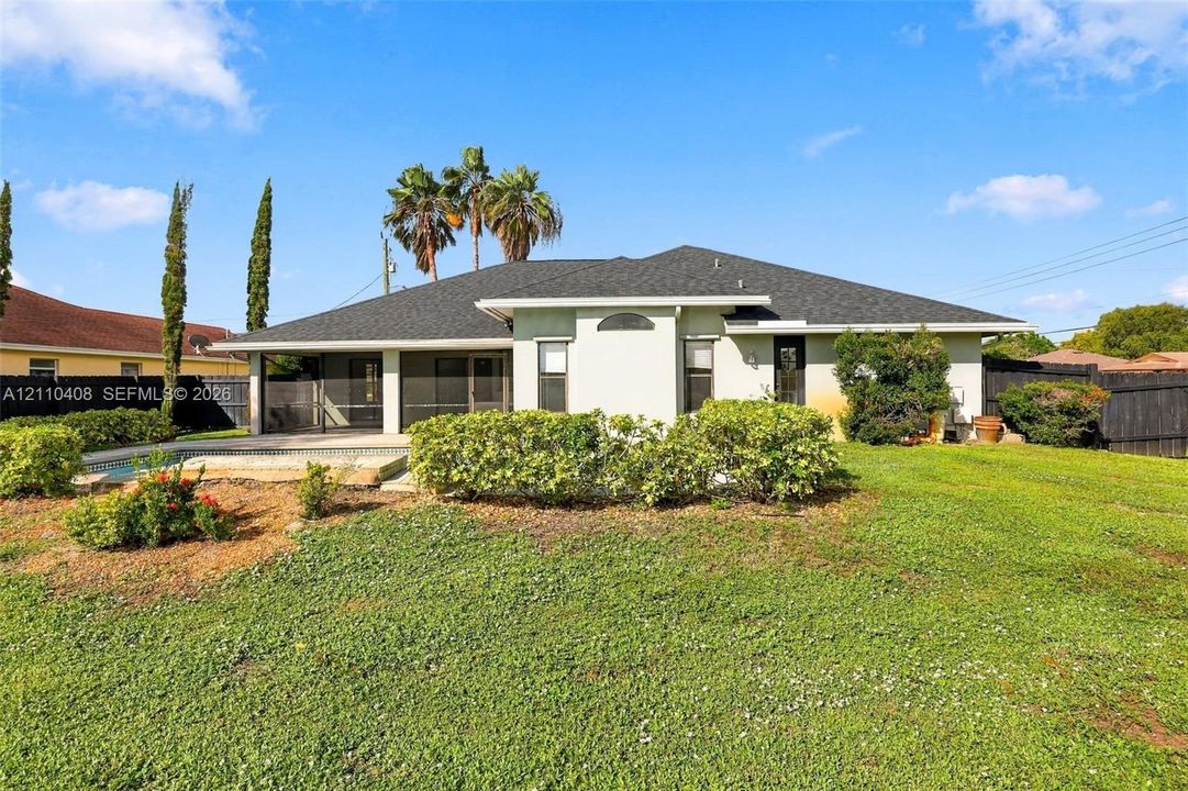 Stucco exterior residence featuring a dark shingle roof, a screened-in lanai, an inground pool, and a perimeter privacy fence situated on a spacious lot