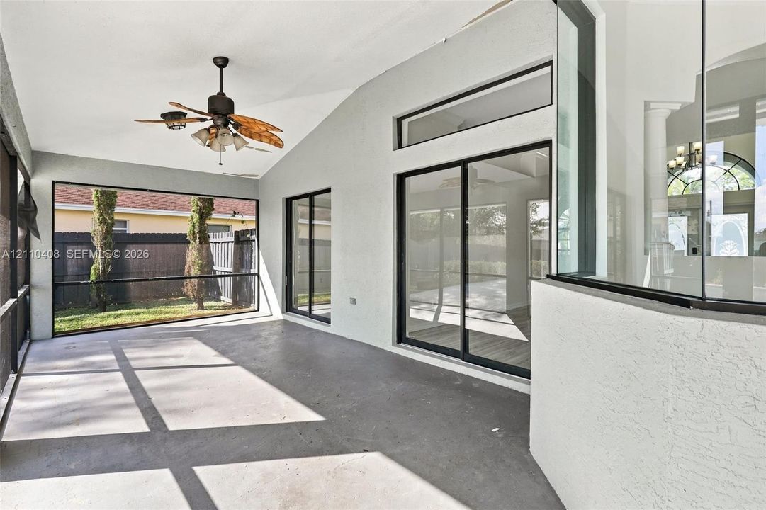 Screened-in patio featuring concrete flooring, a vaulted ceiling, a ceiling fan with integrated lighting, and multiple sliding glass door access points