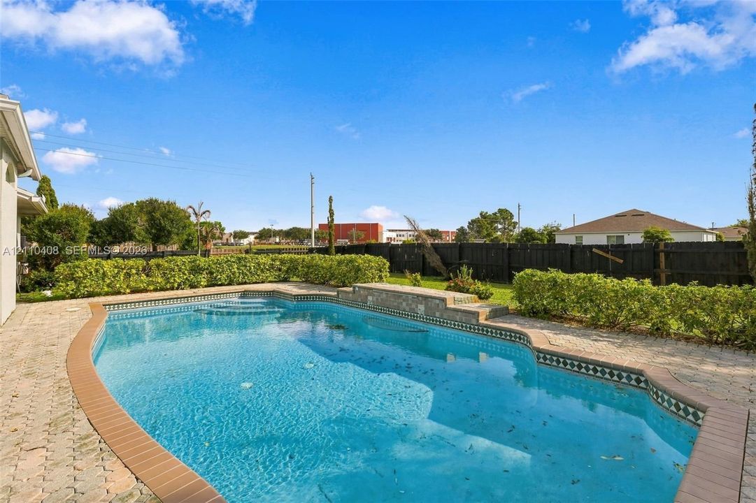 In-ground swimming pool featuring a tiered stone coping, tile border, and concrete paver decking surrounded by hedge landscaping and wood privacy fencing