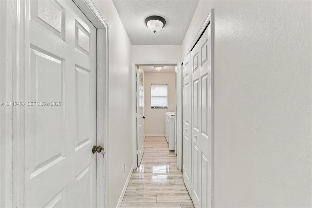 Hallway featuring light-toned tile flooring, flush-mount ceiling light fixtures, and white six-panel interior doors with matching bi-fold closet doors