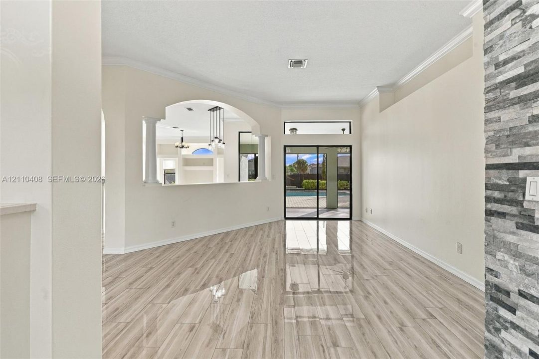 Wood-finish tile flooring, stacked stone wall accent, arched cutout with architectural columns, and sliding glass doors with transom window