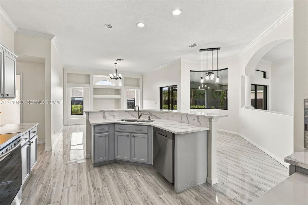 Kitchen featuring a peninsula with solid-surface countertops, grey cabinetry, stainless steel dishwasher, wood-finish flooring, and built-in shelving
