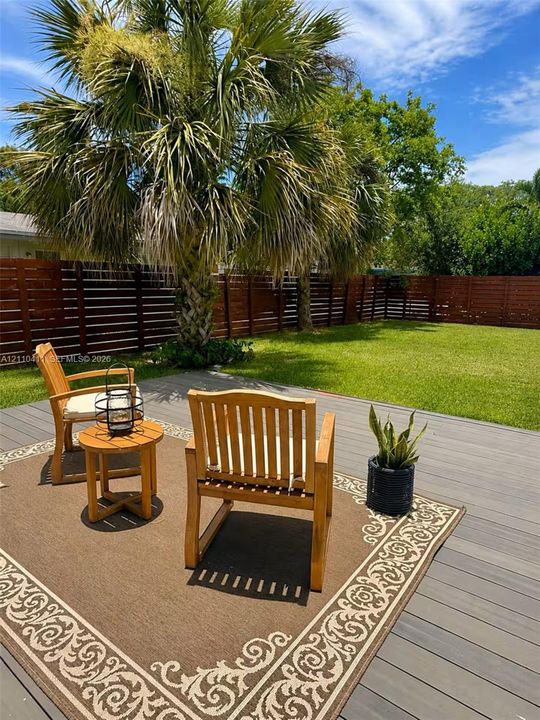 Backyard featuring a composite deck, horizontal slat wood privacy fencing, a mature palm tree, and a manicured lawn