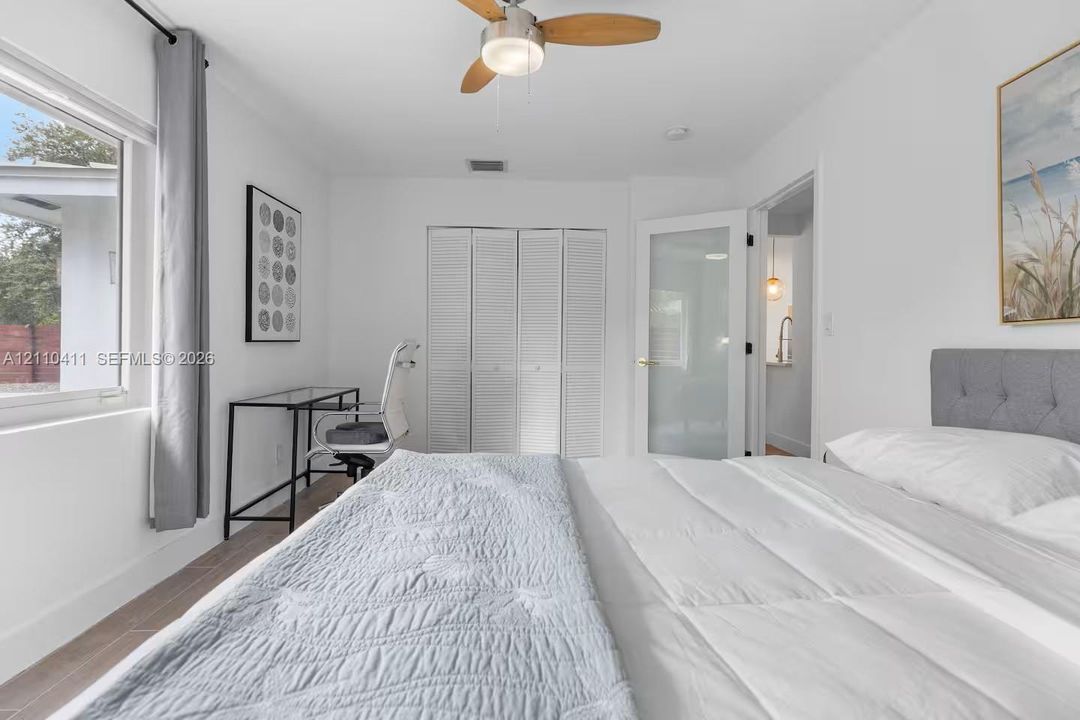 Room featuring wood-finish flooring, a ceiling fan with integrated lighting, white louvered closet doors, and a frosted glass panel door