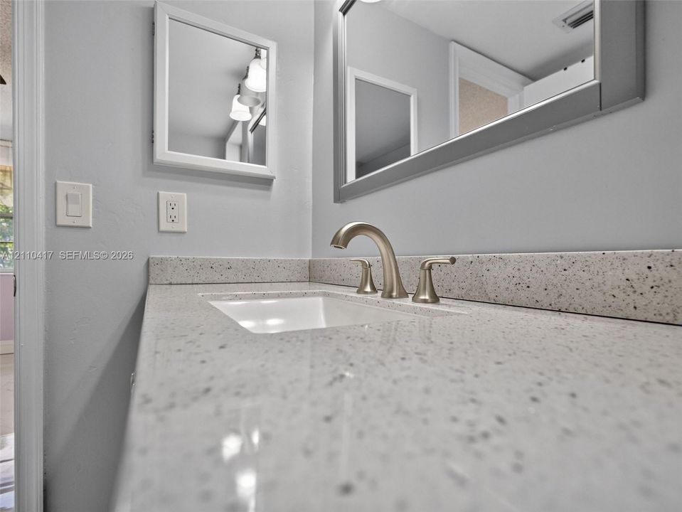 Vanity featuring a speckled stone-composite countertop, integrated rectangular undermount sink, three-piece arched faucet, large wall-mounted mirror, and medicine cabinet