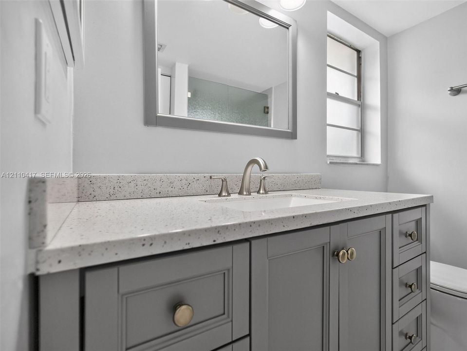 Grey shaker-style vanity featuring a light-toned speckled countertop, undermount sink, brushed nickel faucet, and integrated mirror