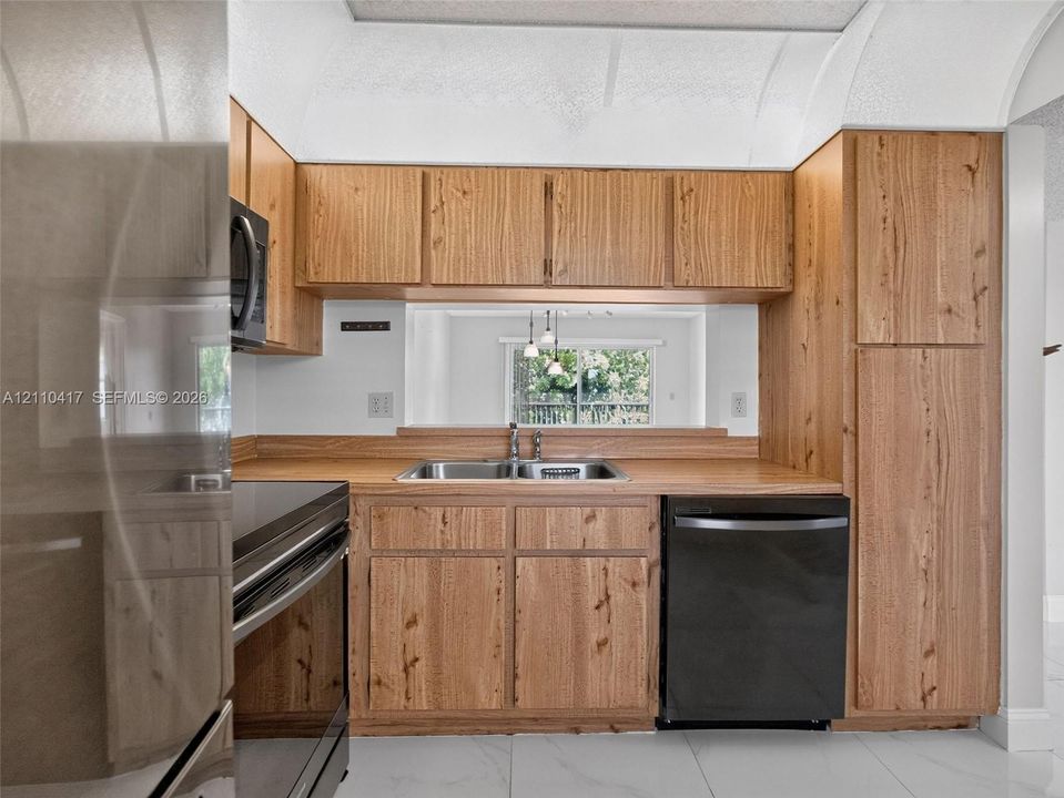 Kitchen featuring natural wood-finish cabinetry, a dual-basin stainless steel sink, black appliances, and white stone-patterned flooring