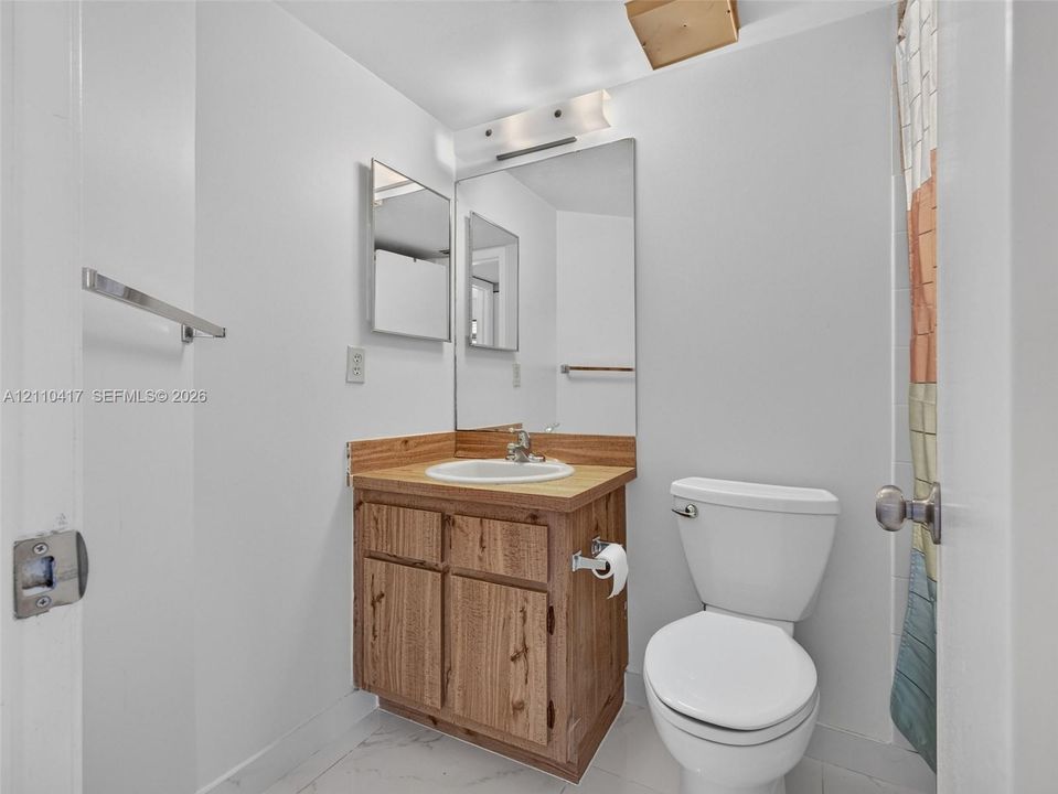 Bathroom featuring a wood-finish vanity with a drop-in sink, solid-surface countertop, full-width mirror, and three-light fixture
