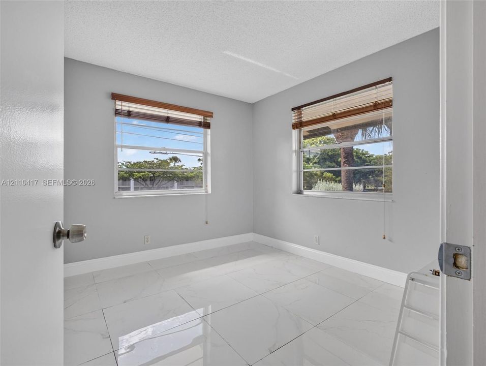 Neutral-toned interior featuring large-format tile flooring, textured ceilings, and dual windows with built-in horizontal blinds