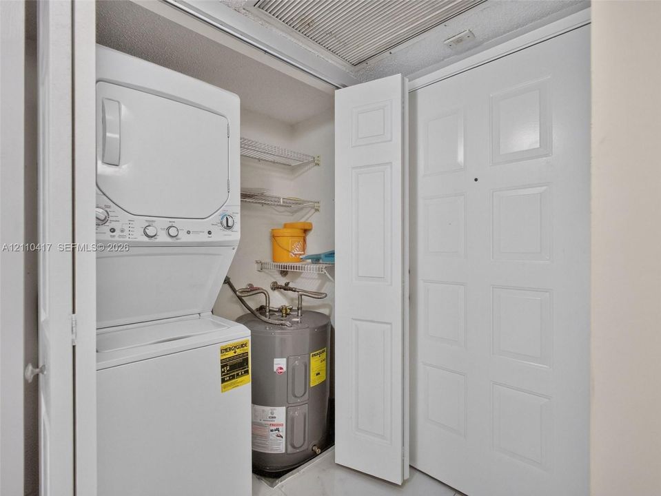Utility closet featuring a stacked washer and dryer, integrated electric water heater, and wire shelving