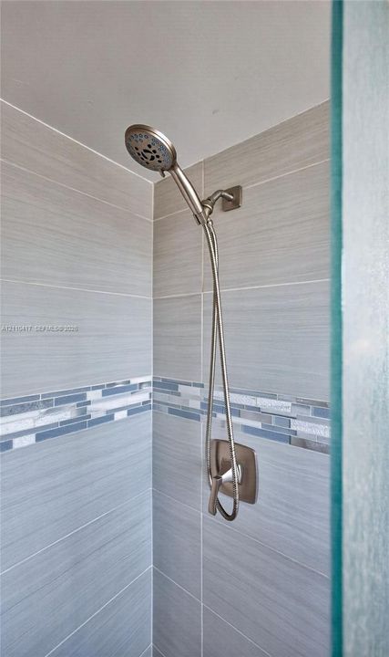 Shower enclosure featuring brushed nickel handheld showerhead, single-handle pressure balance valve, horizontal neutral-toned wall tile, and decorative glass mosaic accent border
