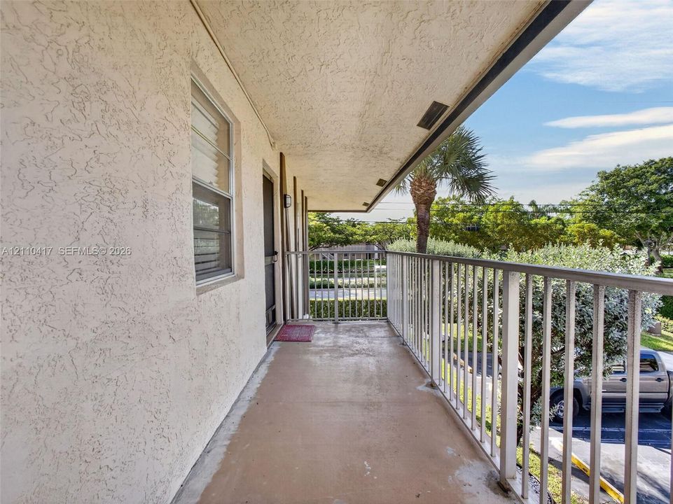 Covered outdoor balcony featuring textured stucco exterior walls, smooth concrete flooring, and metal railings